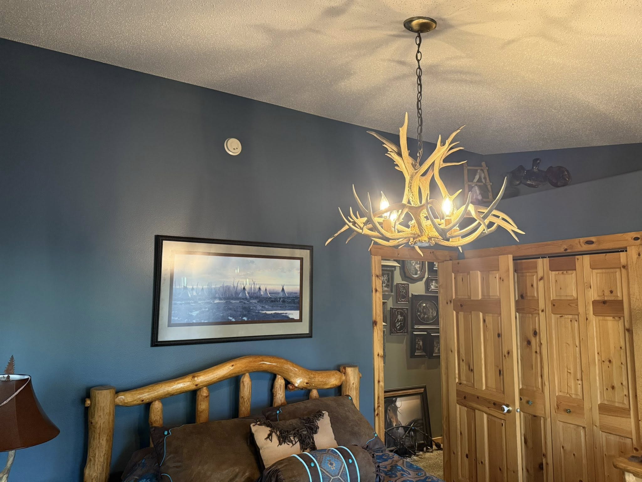 Bedroom with blue-gray painted walls, an antler chandelier, and a log bed