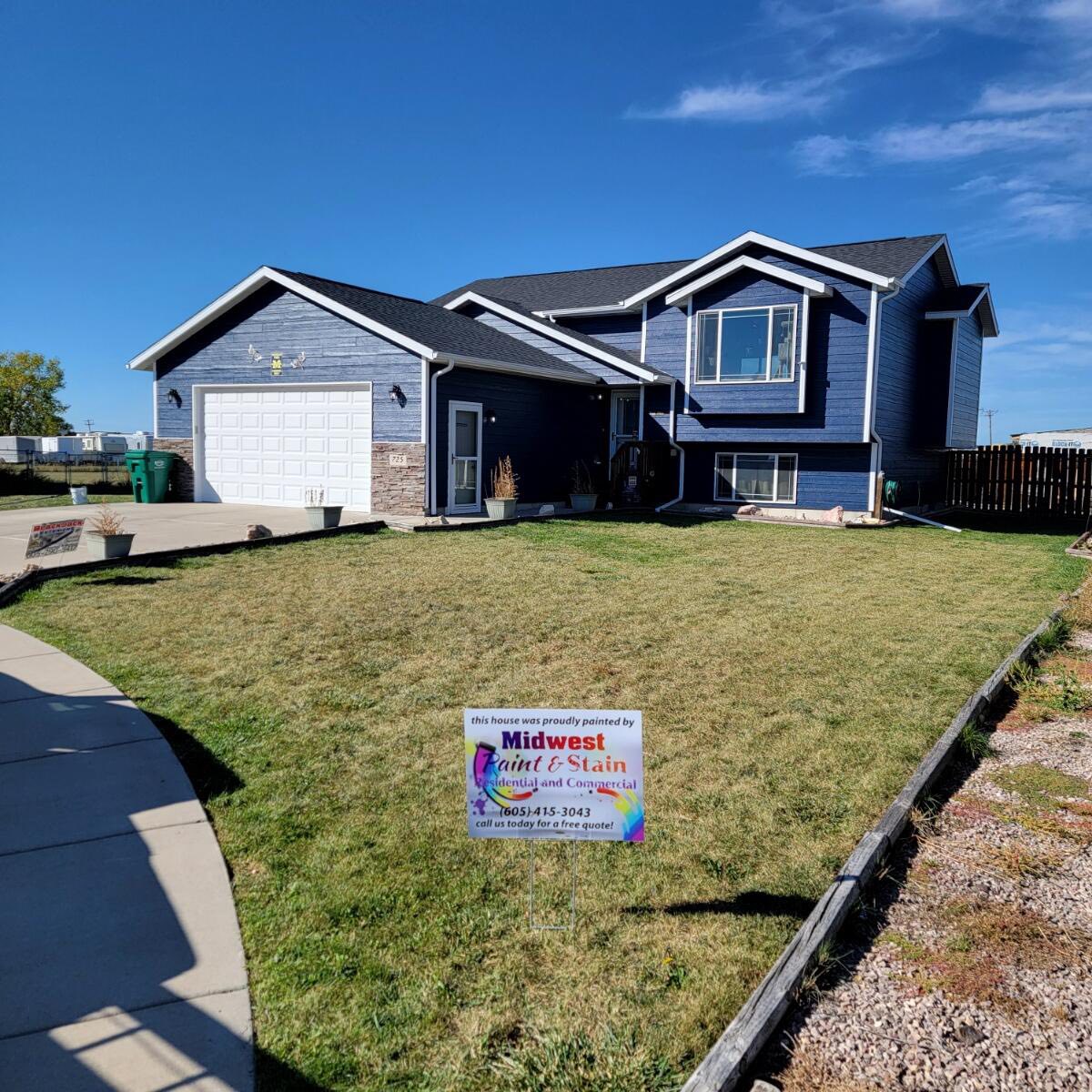 Navy-blue split-level home freshly painted, with a Midwest Paint and Stain yard sign